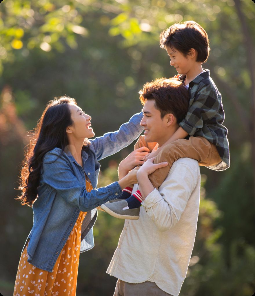 A family smiling together outdoors, a child on a parent's shoulders
